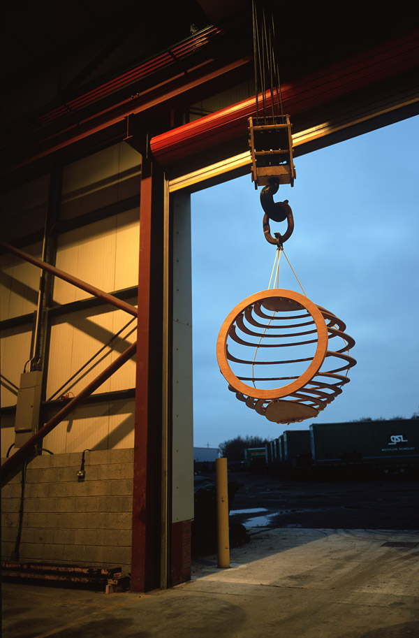 A Hive quite some distance in the air, hoisted in the air by a crane, within the confines of a high-ceilinged warehouse