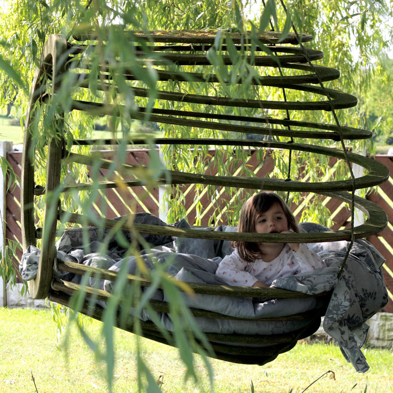 A Hive chair hanging outside in a garden, with Nick's eight year old niece sat inside, lost in her thoughts, furniture design, woodworking, natural finishes, no-one know's what she's thinking...